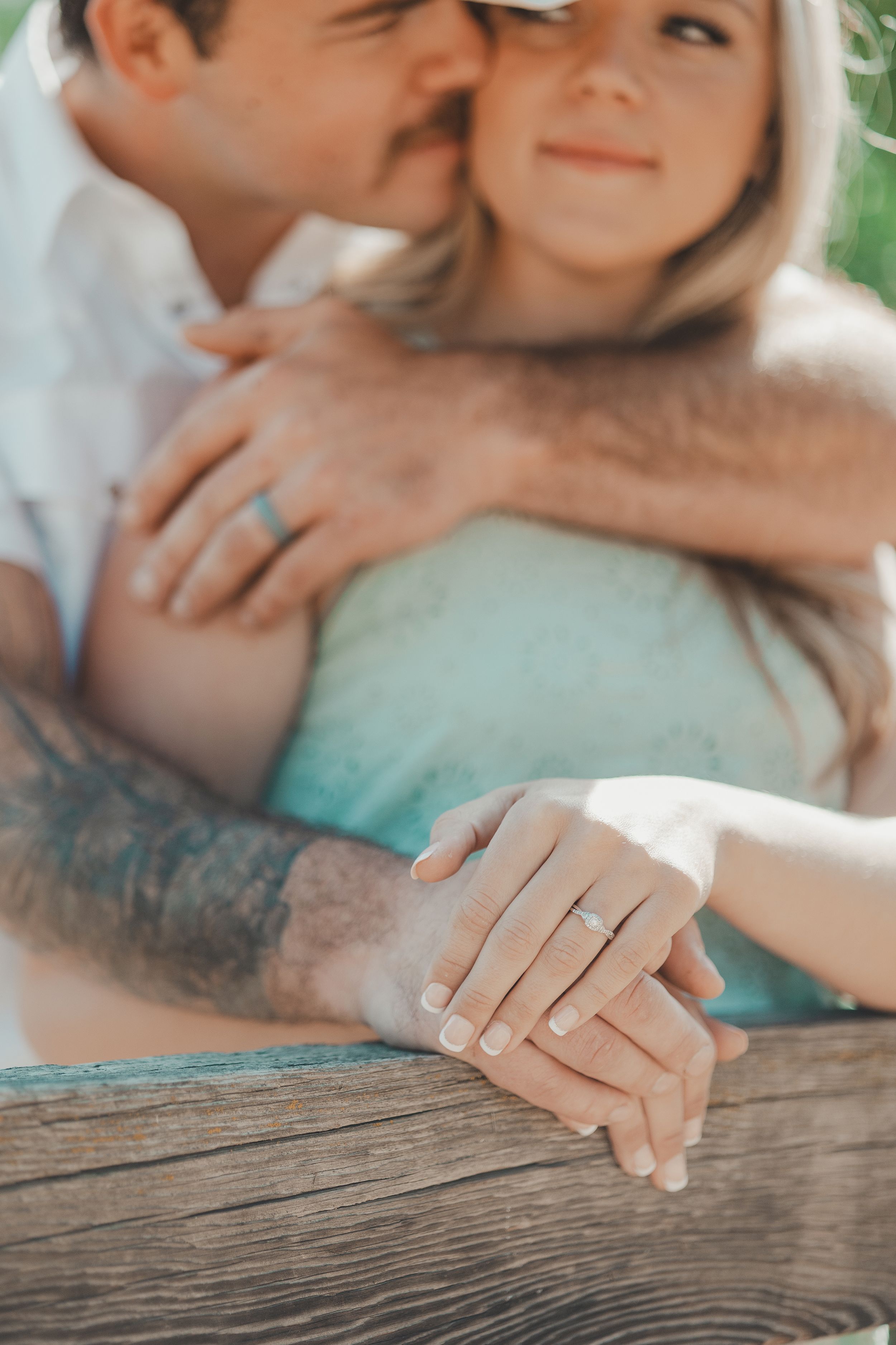 Close-up of hands with engagement ring against wooden fence during intimate moment.