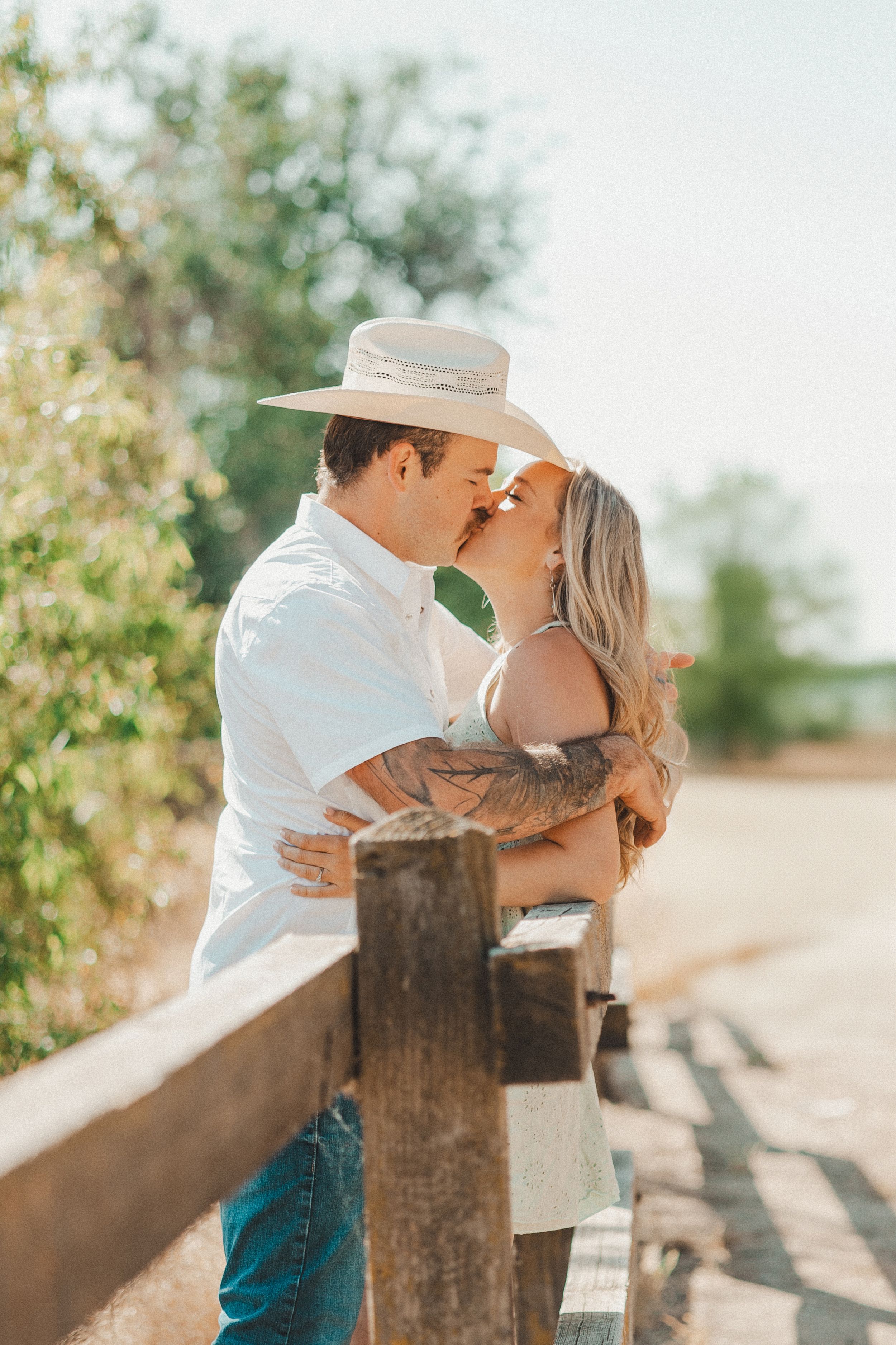 A romantic couple shares an intimate moment by a wooden fence during a golden sunset engagement photoshoot.