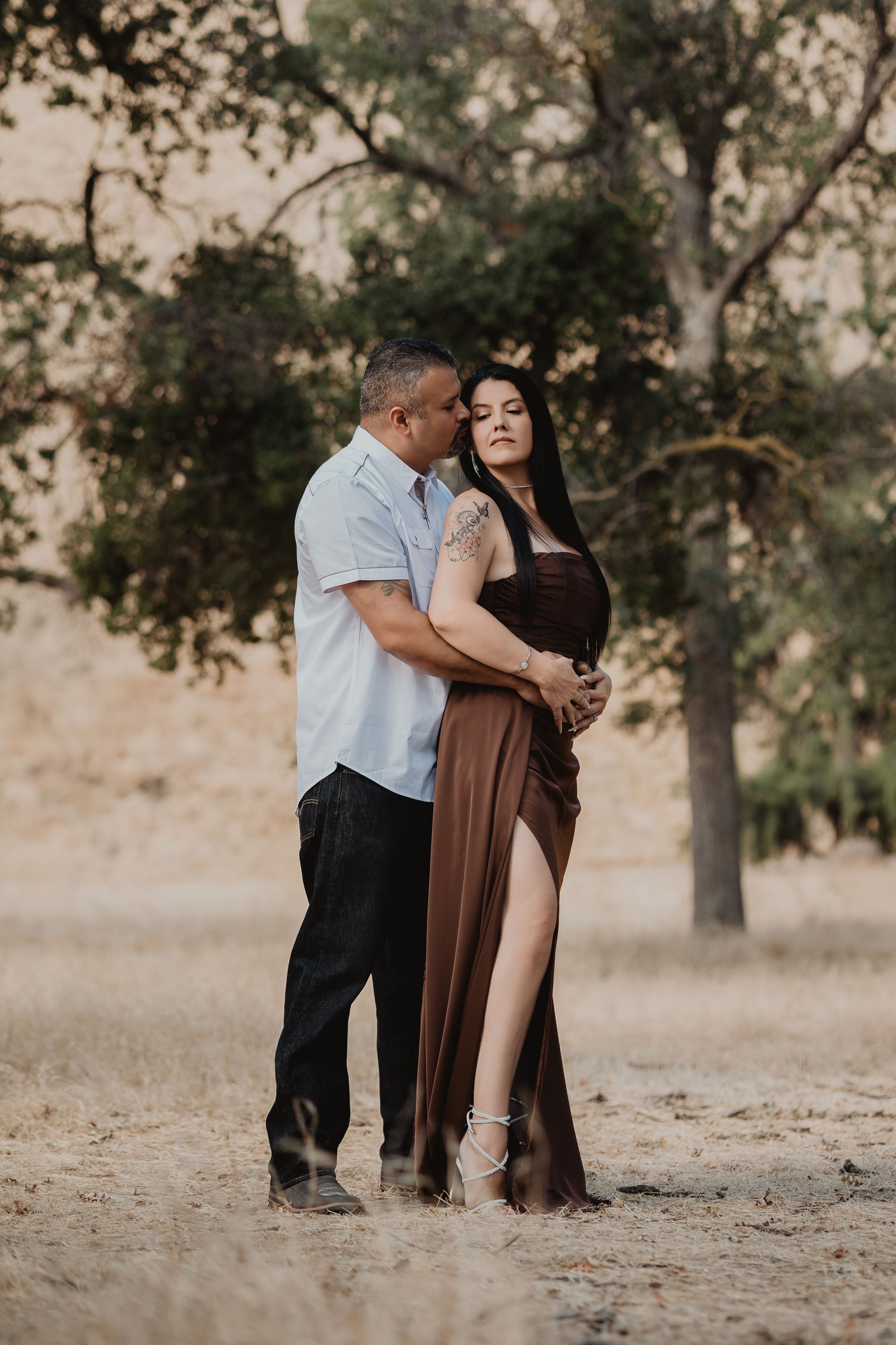 Couple embracing in a romantic pose against a backdrop of trees at golden hour.
