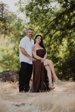 Couple posing together in an outdoor setting with green trees and golden grass.
