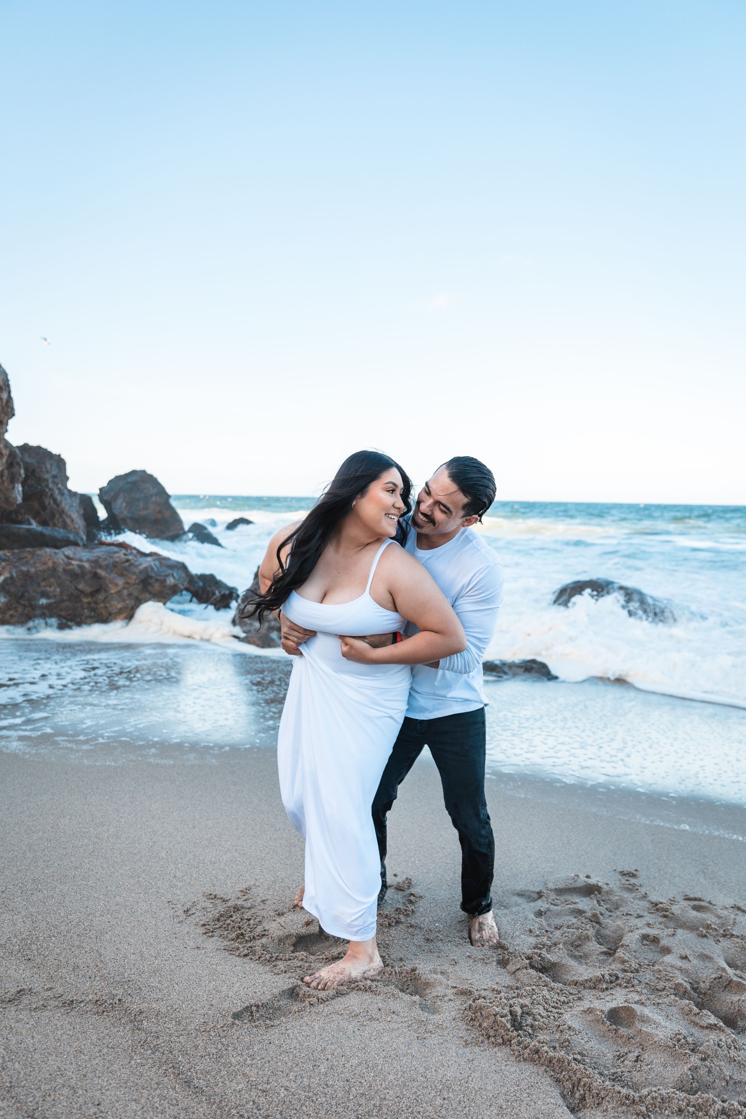 A playful moment between a couple on a rocky beach at sunset.