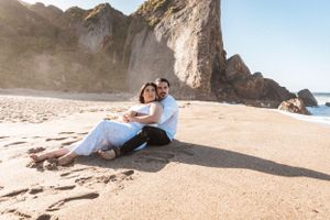 Couple relaxing on sandy beach near dramatic coastal cliffs during sunset.