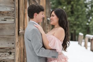 A couple shares an intimate moment while posing against a rustic wooden wall.