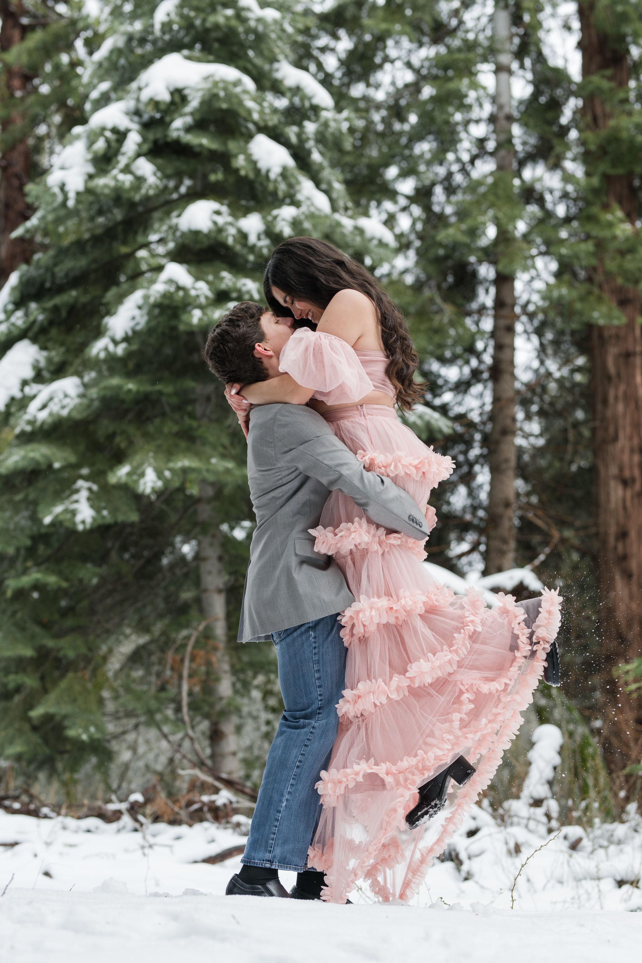 A joyful lift pose captured in a snowy forest setting during an engagement session.