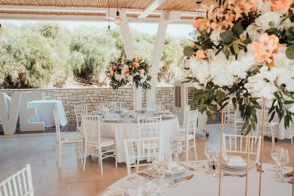 Elegant wedding reception setup with white chiavari chairs and floral centerpieces in bright venue.