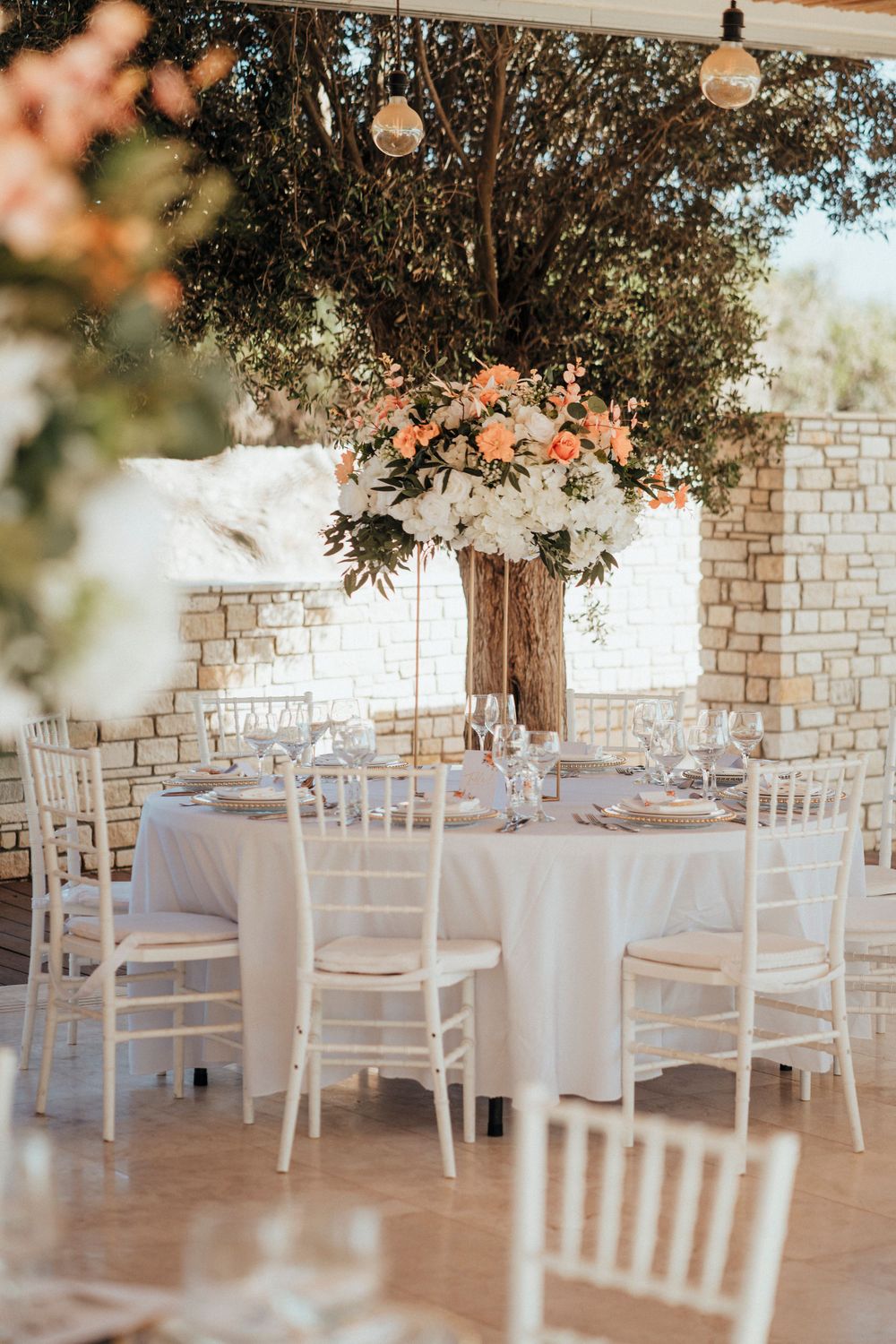 Wedding reception table with white linens and elegant floral centerpiece in rustic stone venue.