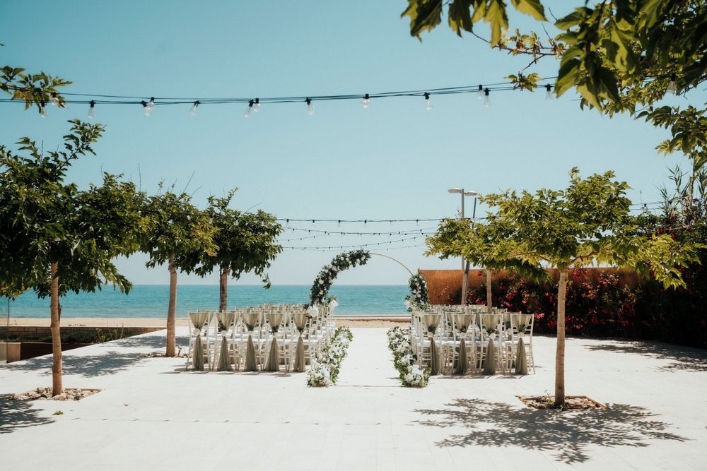 Beach wedding ceremony setup with white chairs and string lights creating an aisle leading to the ocean view.