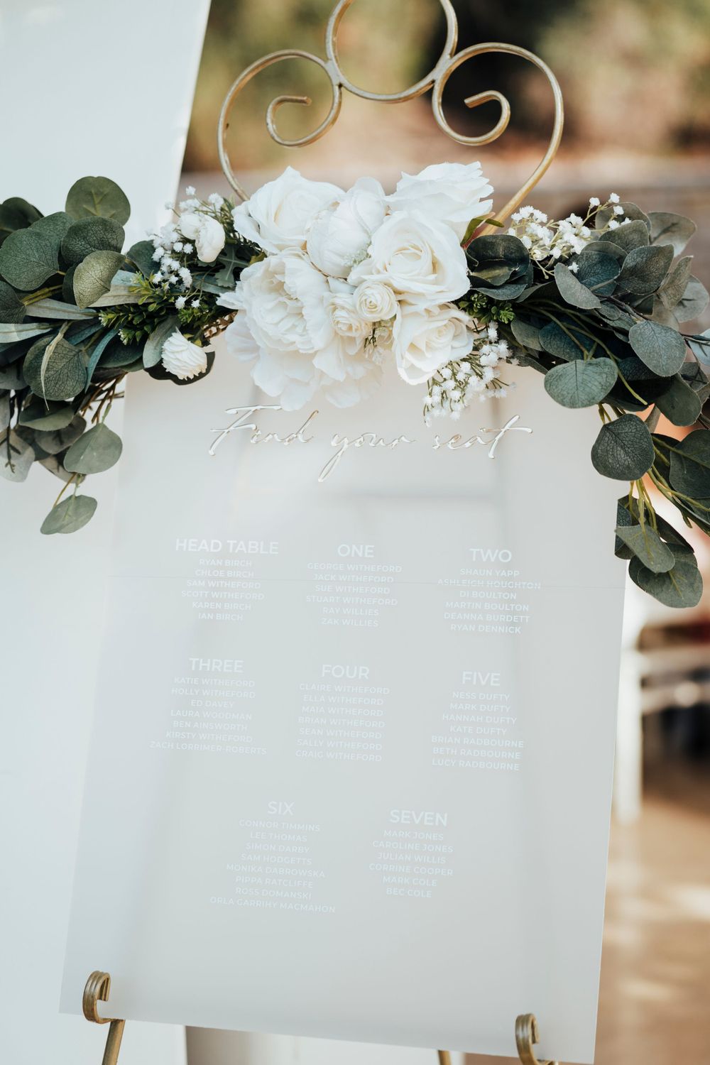 White seating chart decorated with eucalyptus leaves and roses in an elegant display.