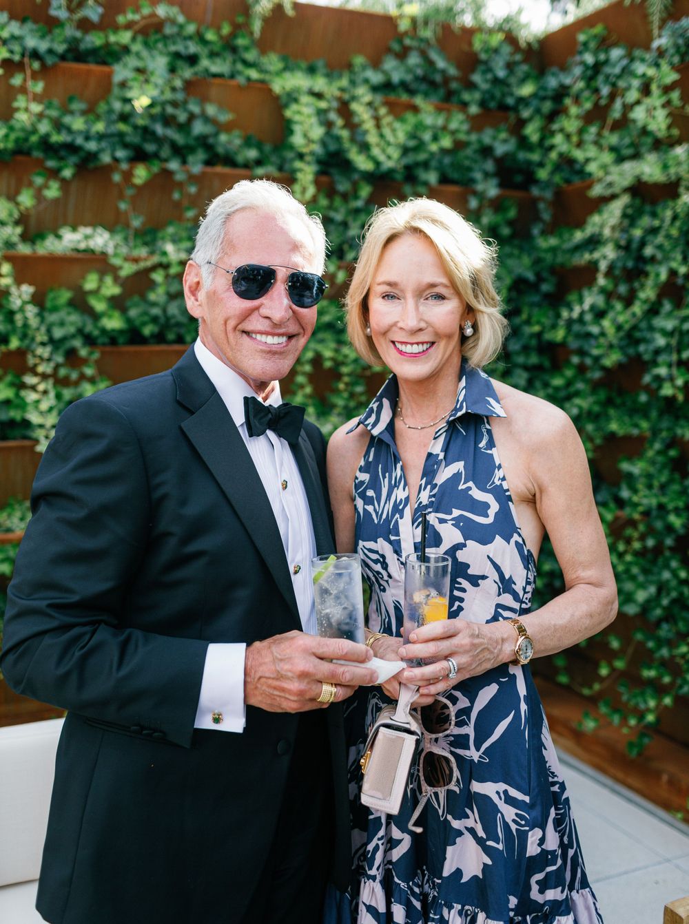 Couple posing in formal attire, enjoying drinks against the lush green wall backdrop at Six Senses Douro Valley.
