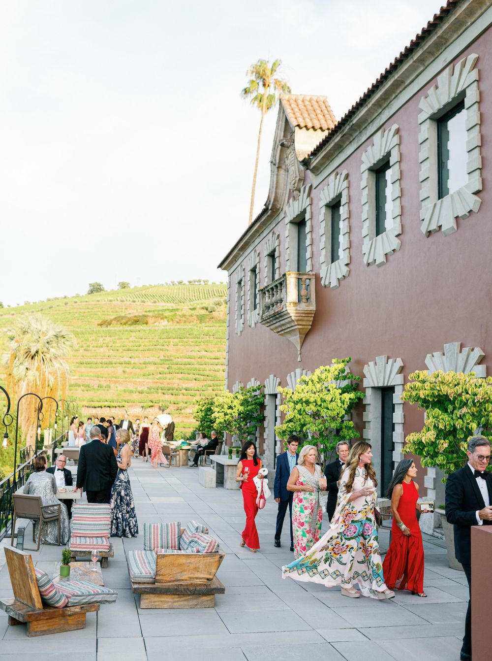 Elegant guests dressed in colorful attire, enjoying cocktail hour on the villa’s terrace with panoramic vineyard views.