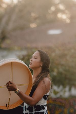 Person holding large tan drum outdoors during golden hour with bokeh background.
