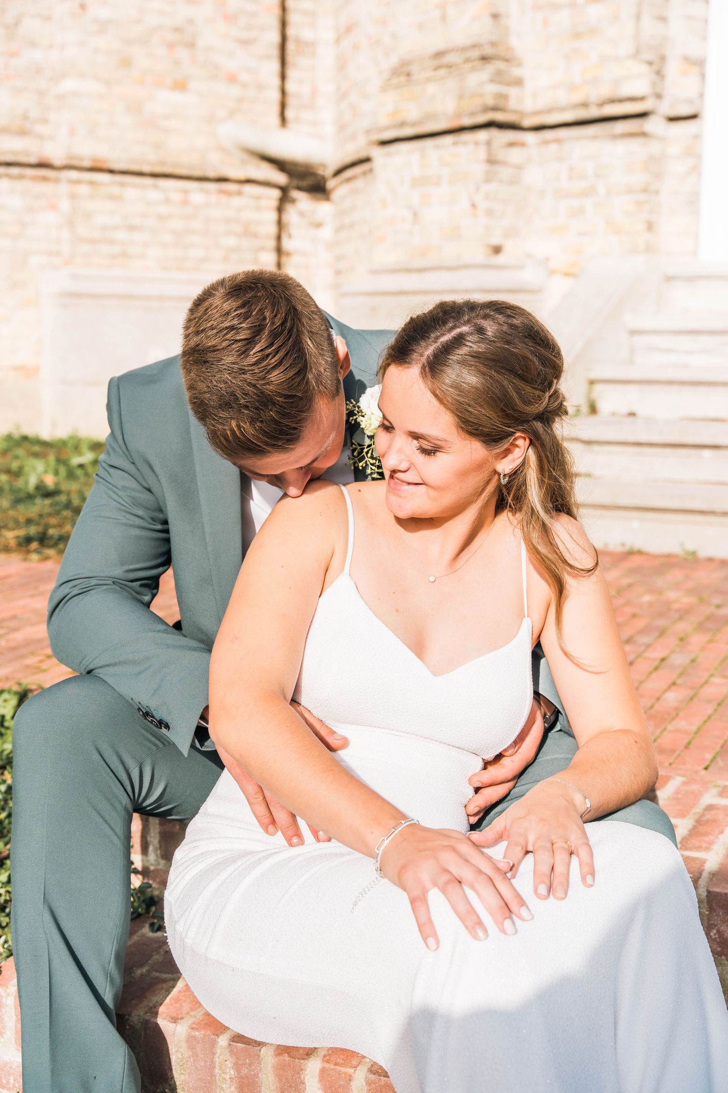 Intimate wedding couple moment on brick steps against stone building backdrop.