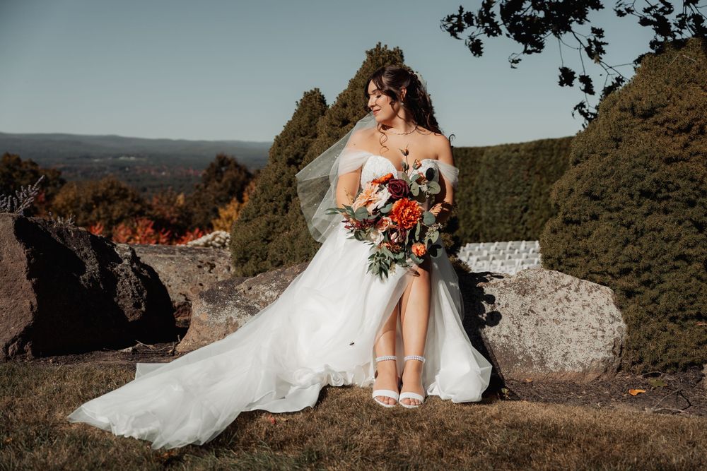 A stunning wedding portrait shows a bride in white perched gracefully on rocky cliffs with mountain views.