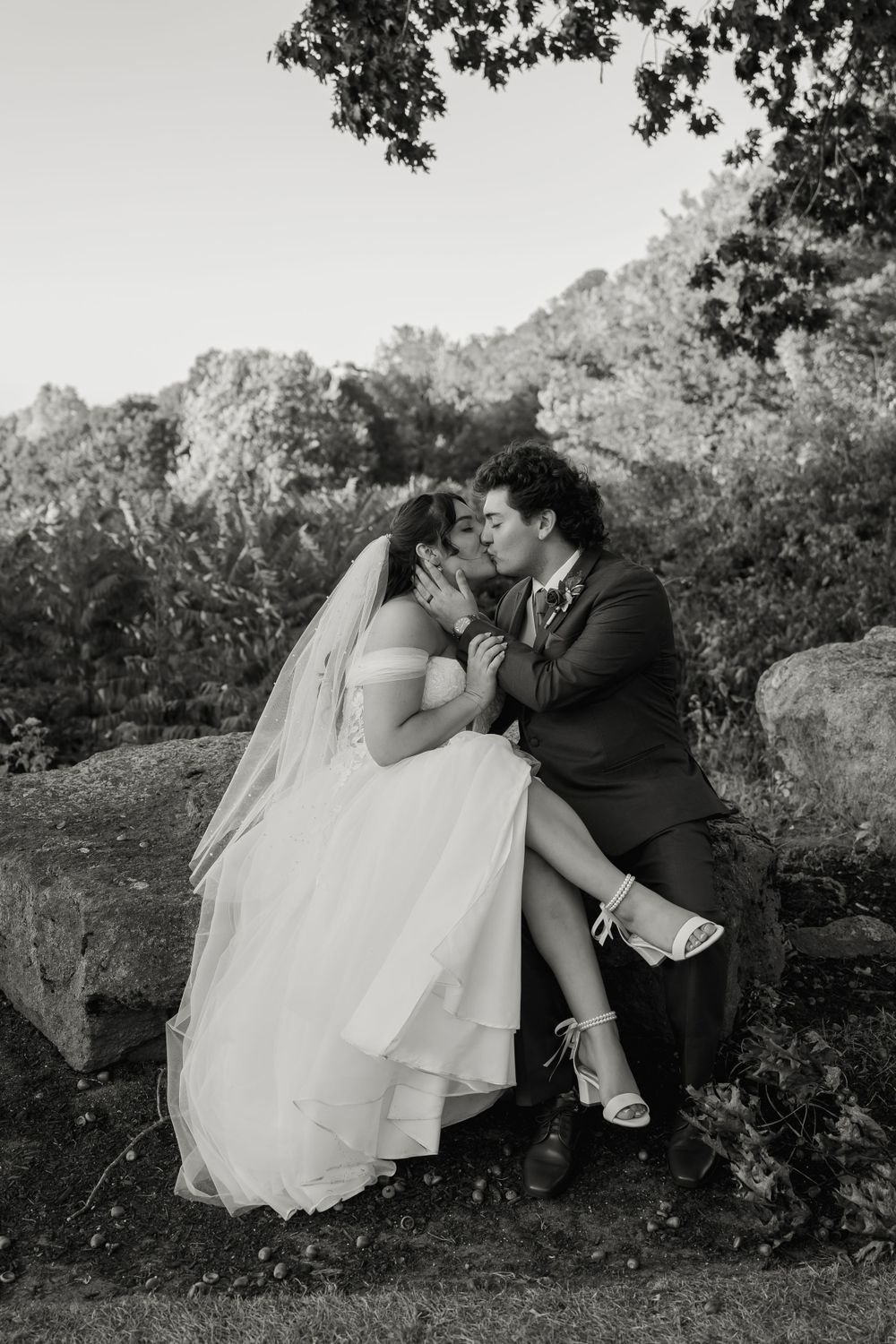 Black and white portrait of couple sharing intimate moment on stone wall.