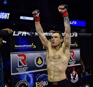 Mixed martial arts fighter celebrating victory with raised arms in octagon during LFA event.