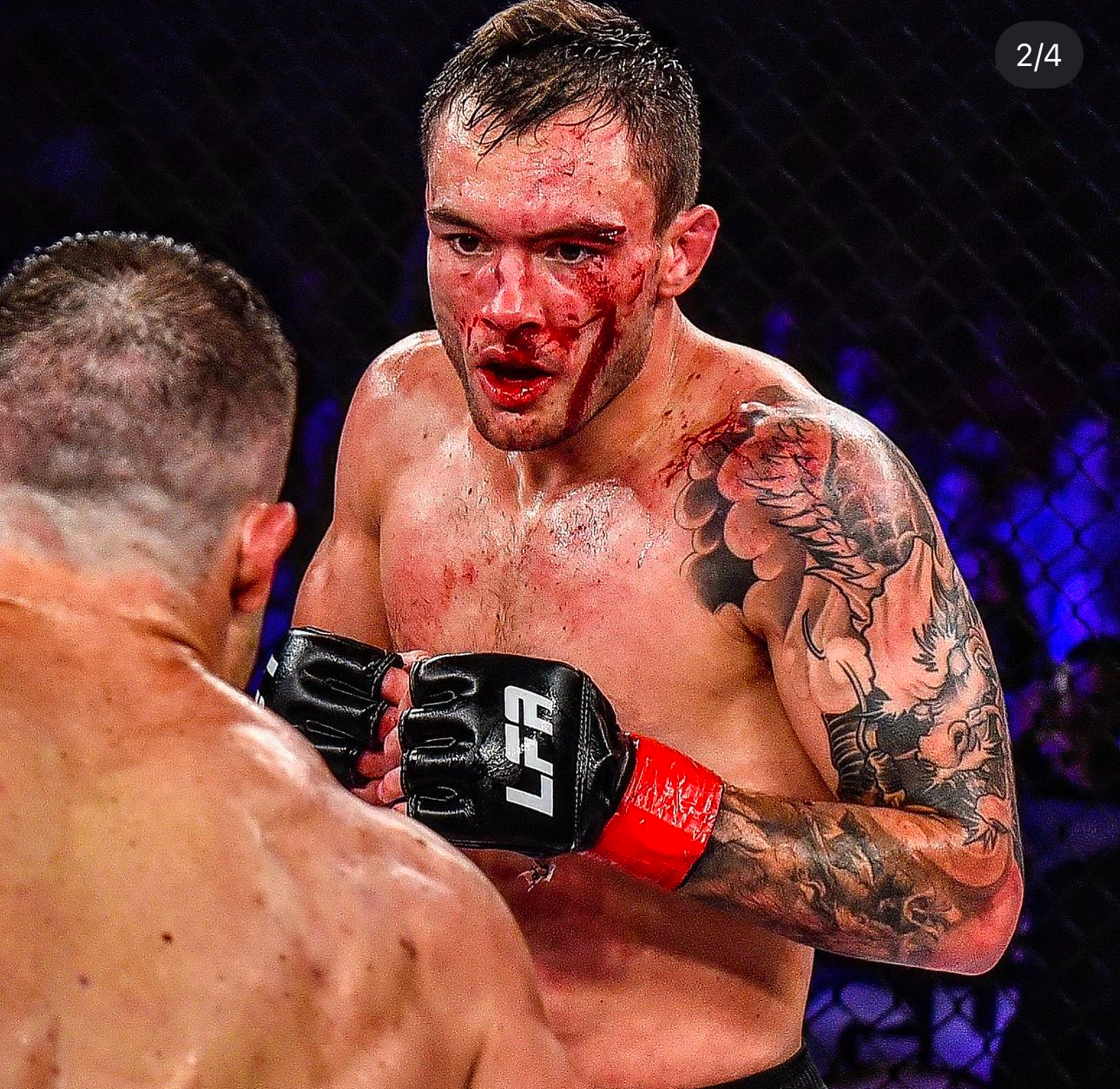 UFC fighter with tattoos and blood on face squares off against opponent in octagon during intense MMA fight match.
