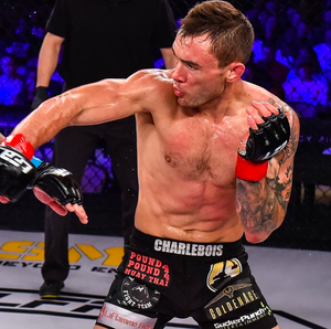 MMA fighter in black shorts throws a powerful punch during a cage fight with blue lighting in the background.