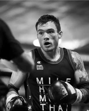 Fighter wearing a Muay Thai tank top holds focus mitts during intense training session.