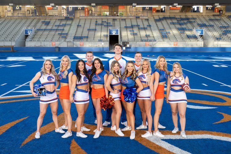Cheerleading squad poses together on blue athletic field with orange and white uniforms at stadium.