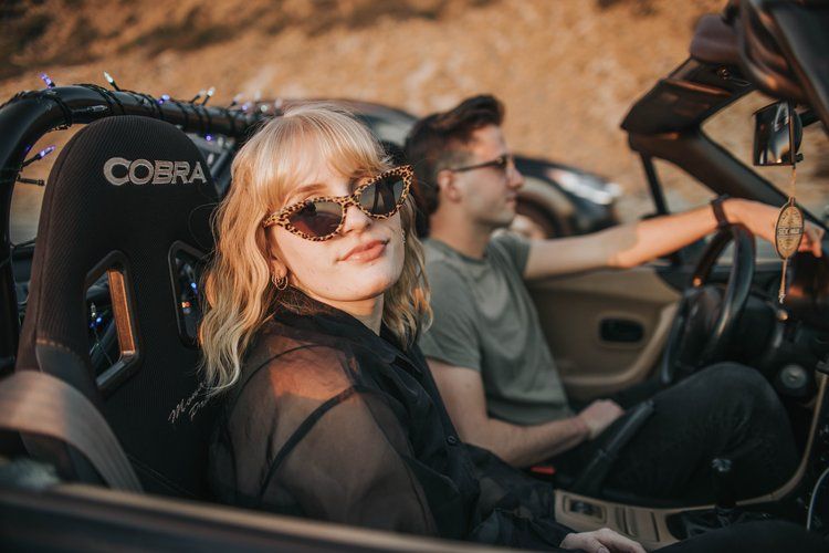 Two people sitting in a sports car with Cobra racing seats during golden hour lighting.