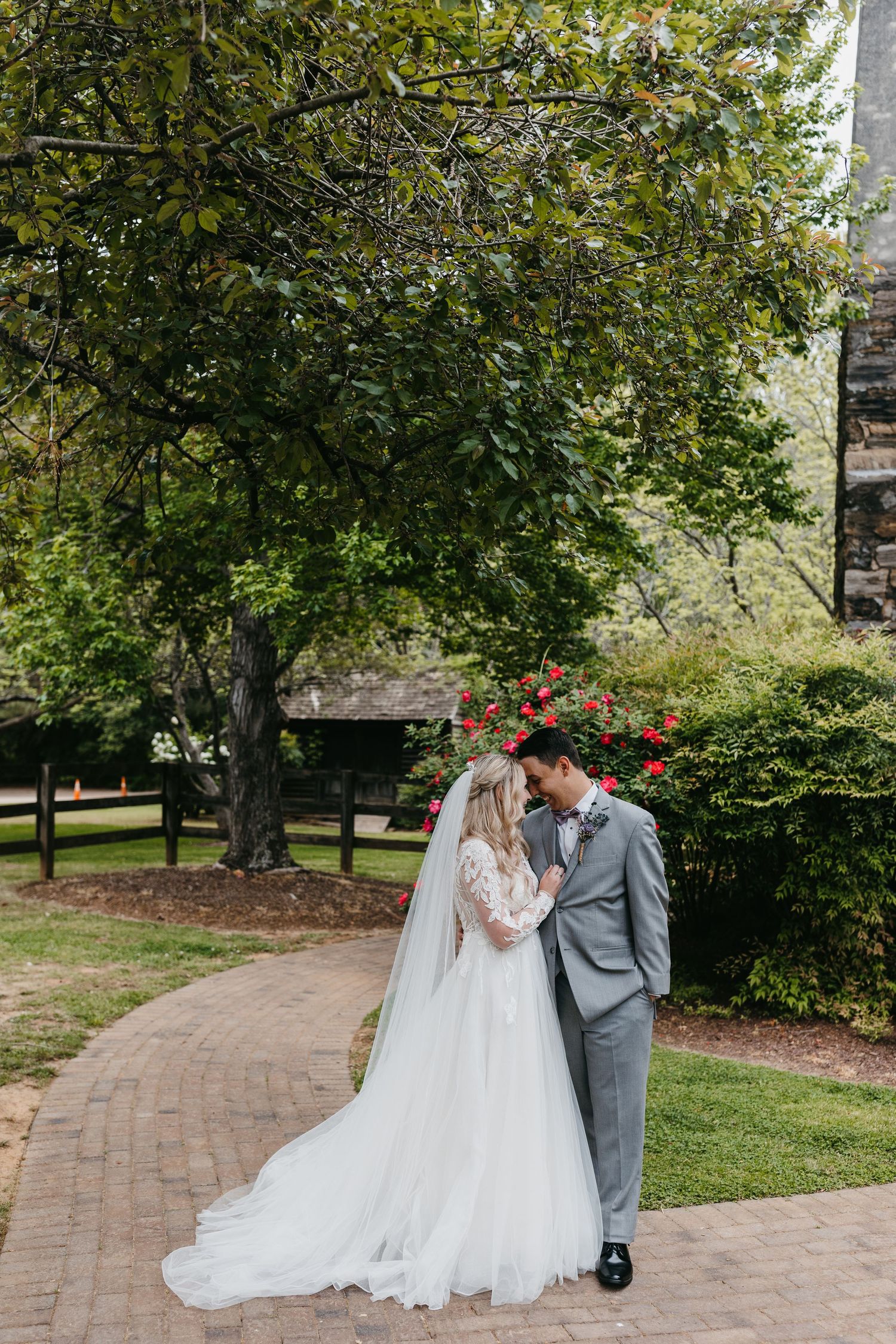 Newlyweds sharing romantic moment on brick path surrounded by trees.