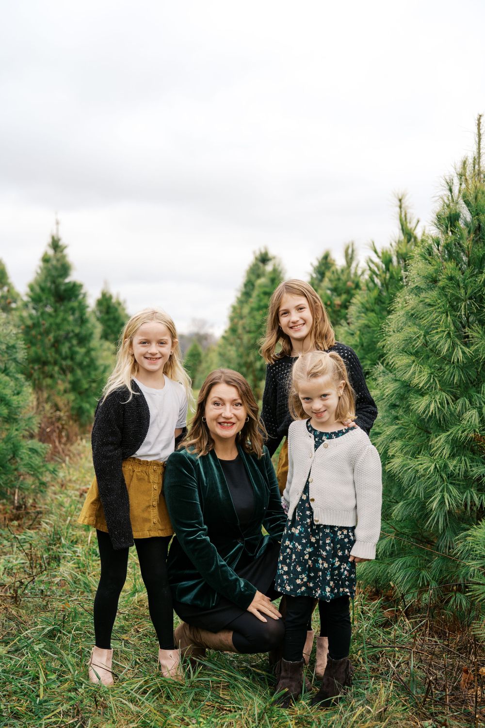 A group portrait among pine trees with matching mustard skirts and dark sweaters.