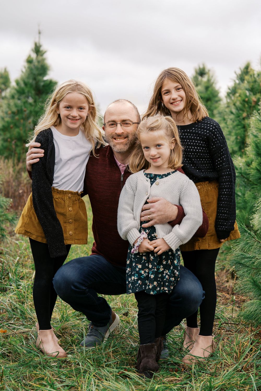 A casual family portrait taken between rows of evergreen trees on an overcast day.