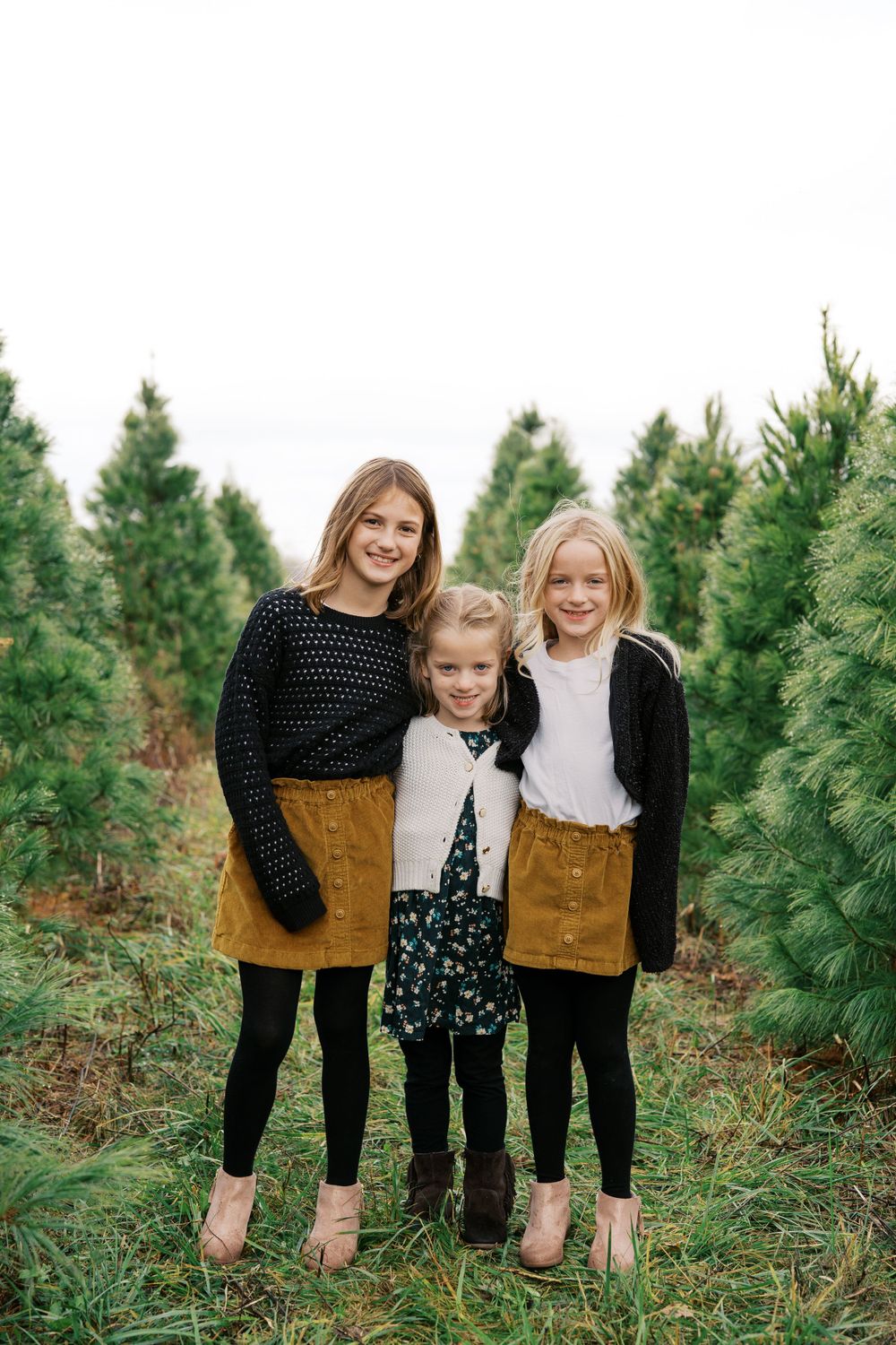 Three people wearing coordinating outfits pose together in a Christmas tree farm.