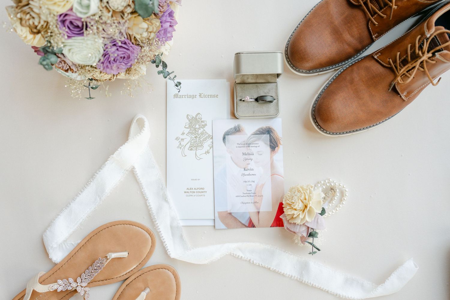 Wedding flat lay with brown leather shoes, invitations, and dried flower bouquet.