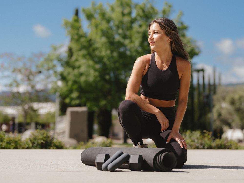 Athletic person in workout gear kneeling on concrete during outdoor exercise session.