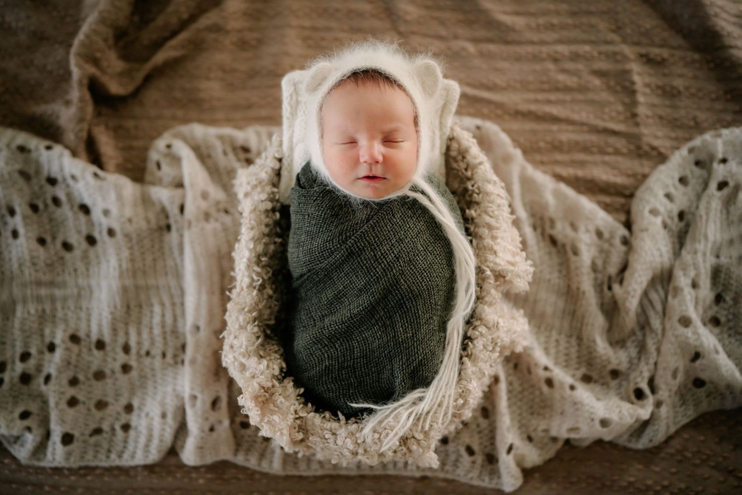 Sleeping baby wrapped in green swaddle rests on patterned blanket.