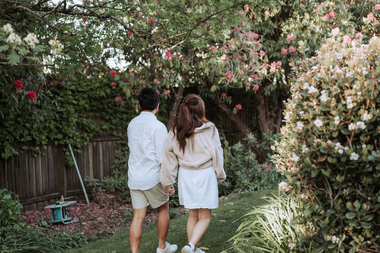 A couple strolls through a blooming garden with white flowers and pink blossoms.