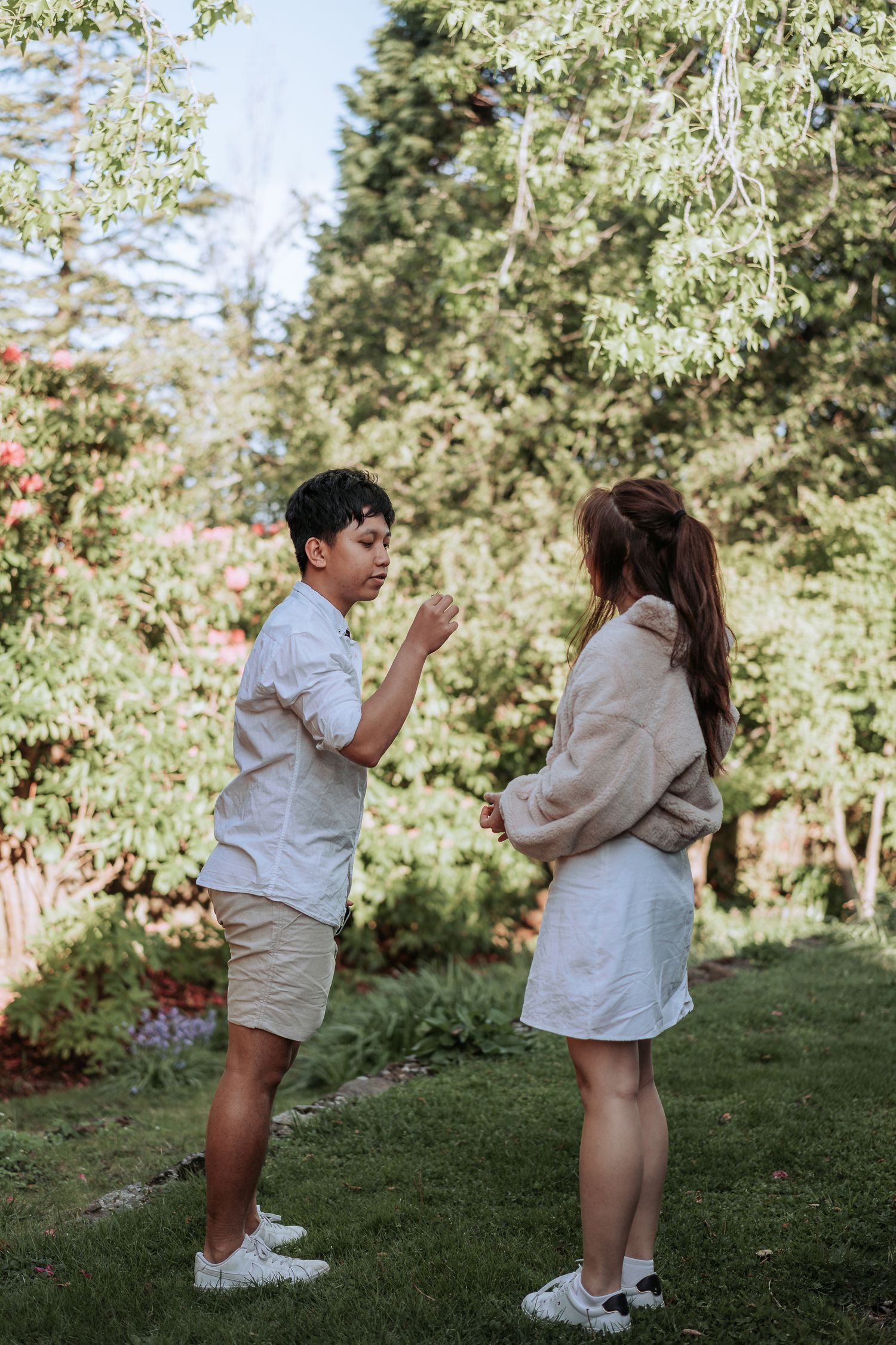 A tender moment unfolds between two people standing on a garden lawn surrounded by blooming trees.