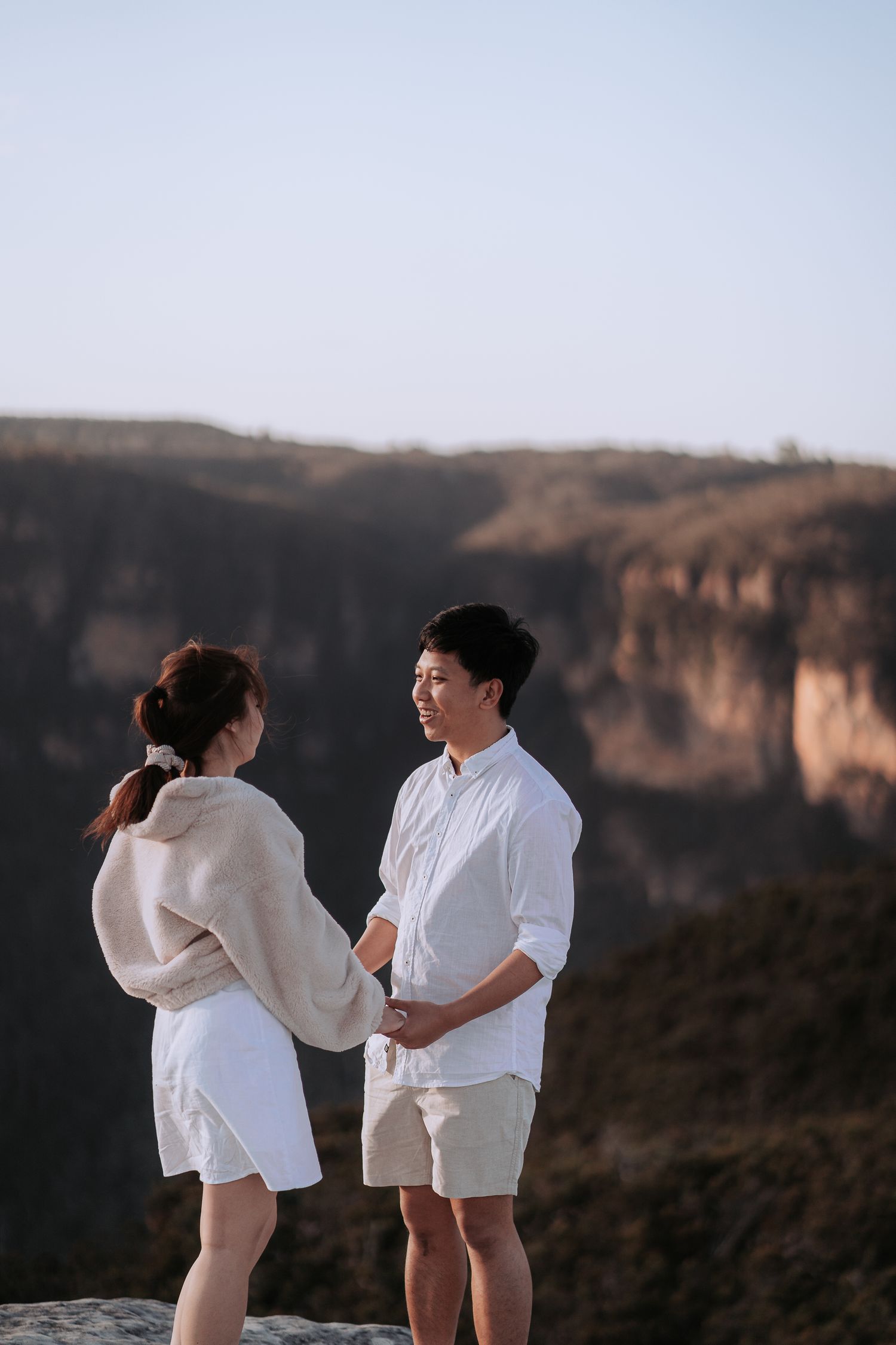 A couple in matching white outfits shares a moment together on a mountain overlook.