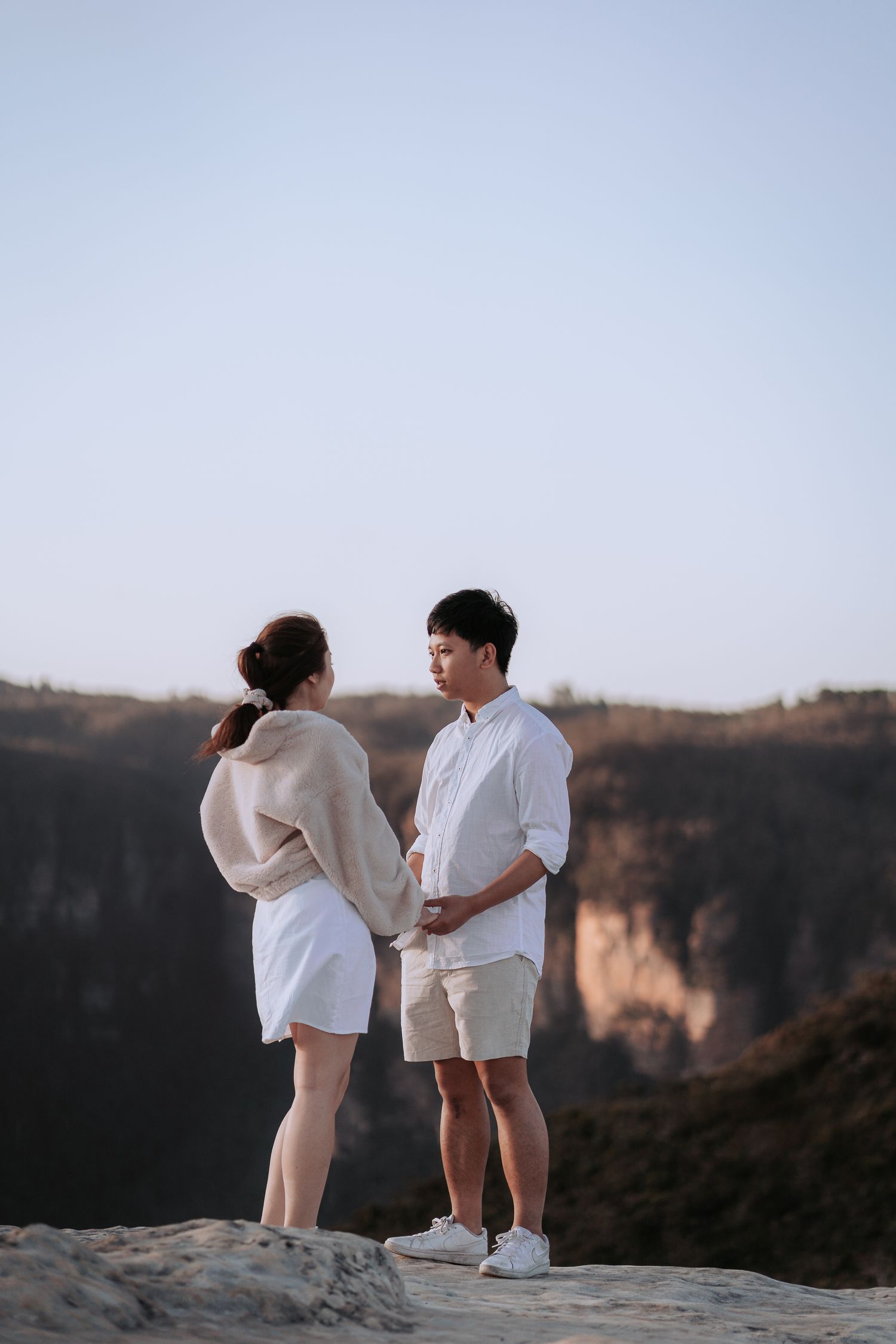 A couple stands together on a rocky overlook with dramatic canyon views in the background.