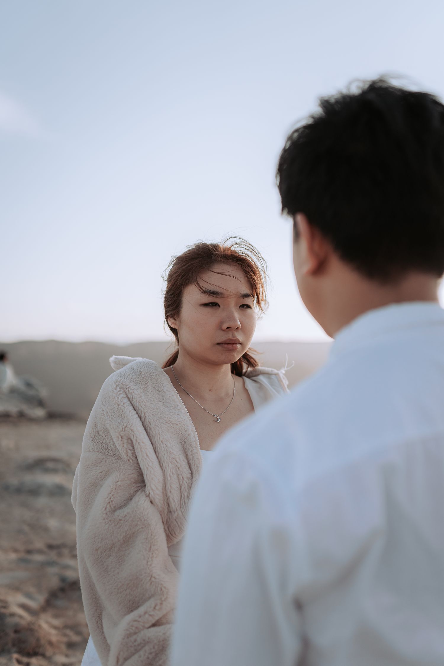 Two people share an intimate conversation on a clifftop with mountains in the background.