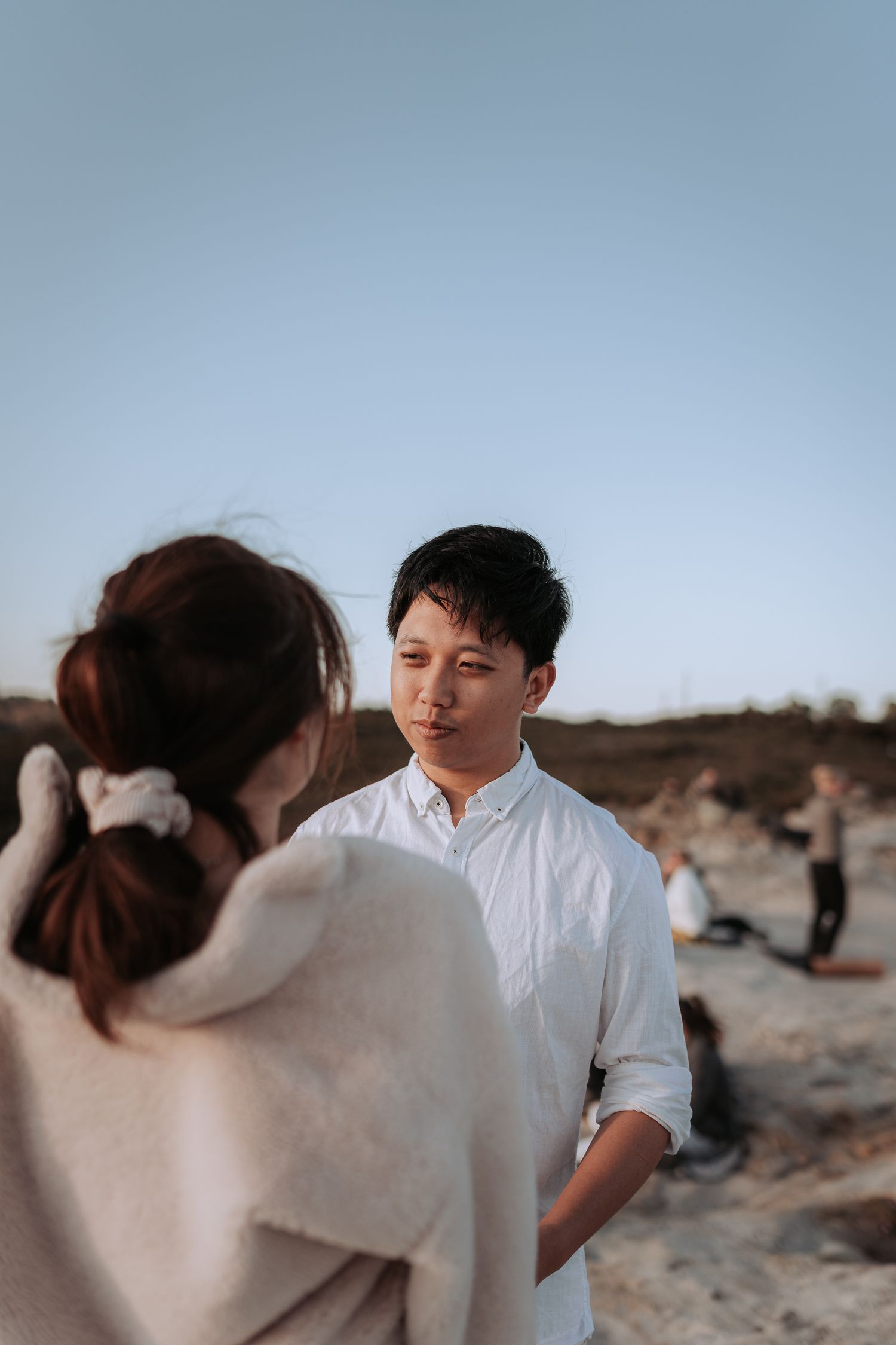 Two people in light colored clothing have a conversation against a dramatic mountain backdrop.