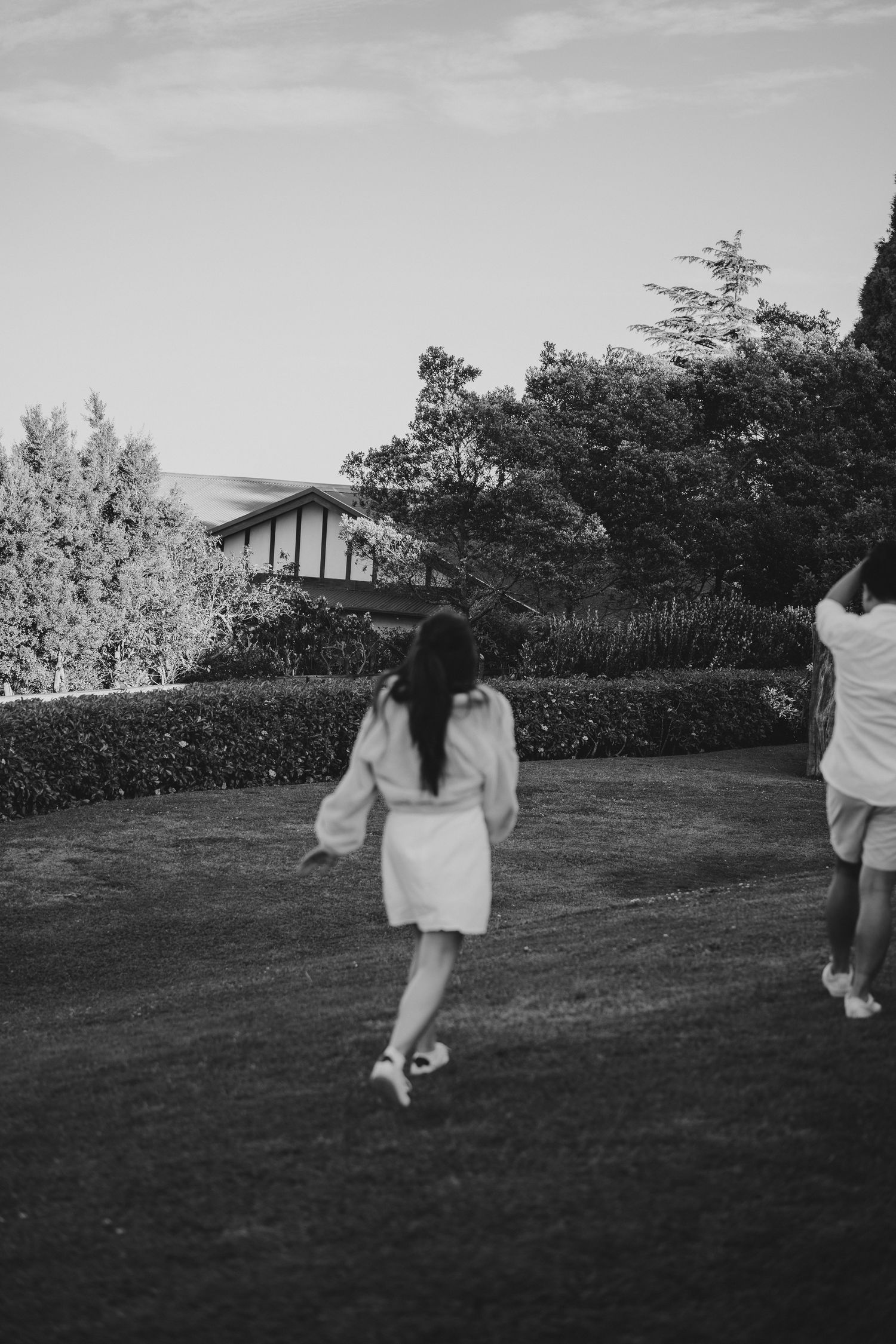 Black and white photo capturing a casual garden scene with figures walking on a grassy lawn.