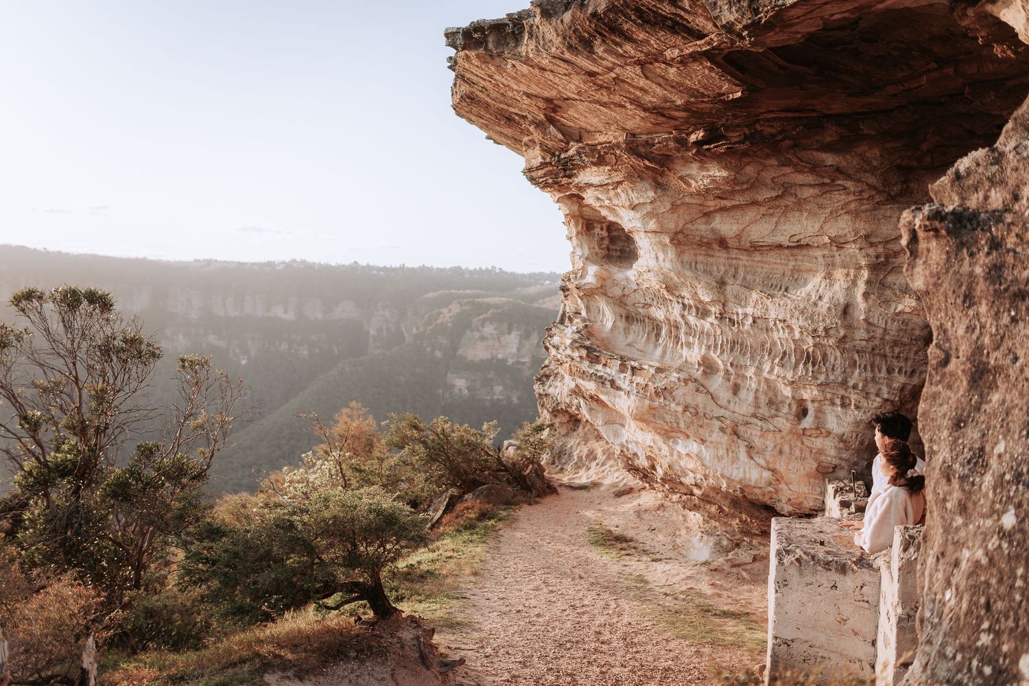 Person standing on a scenic cliff ledge overlooking a vast canyon landscape.