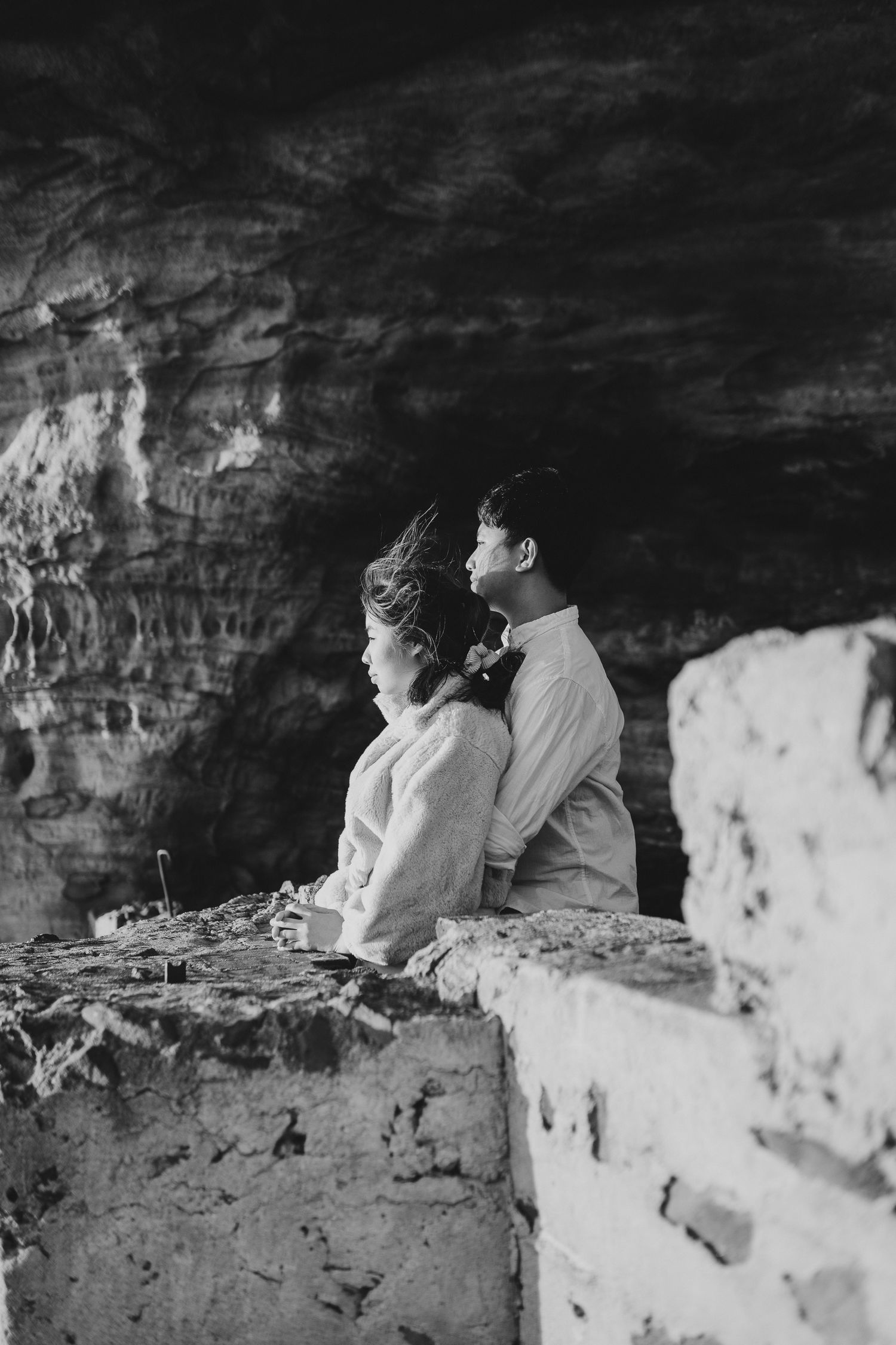 Couple sharing an intimate moment while sitting on a rocky ledge inside a cave.