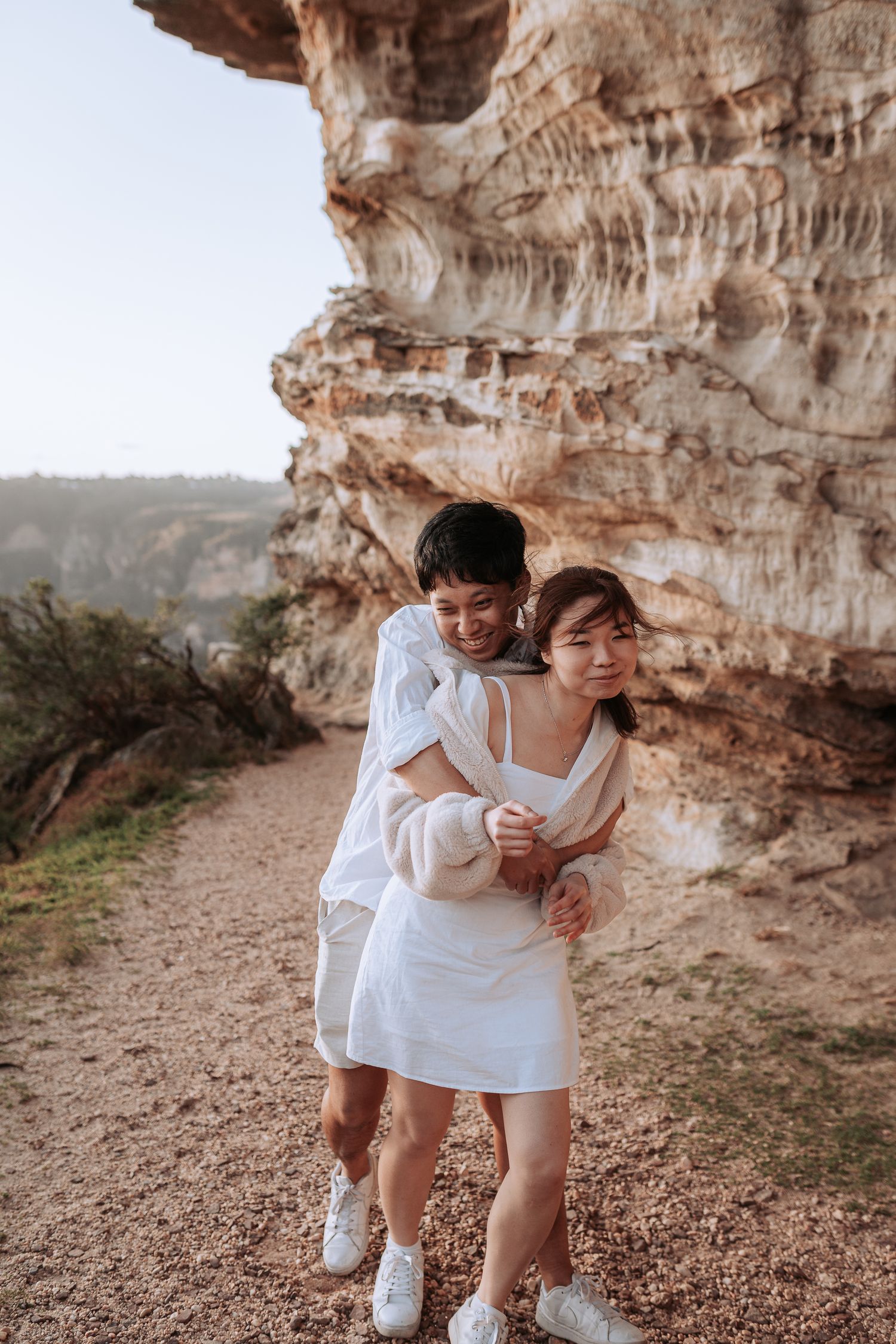 A playful moment captured between a couple in white outfits along a limestone cliff path.