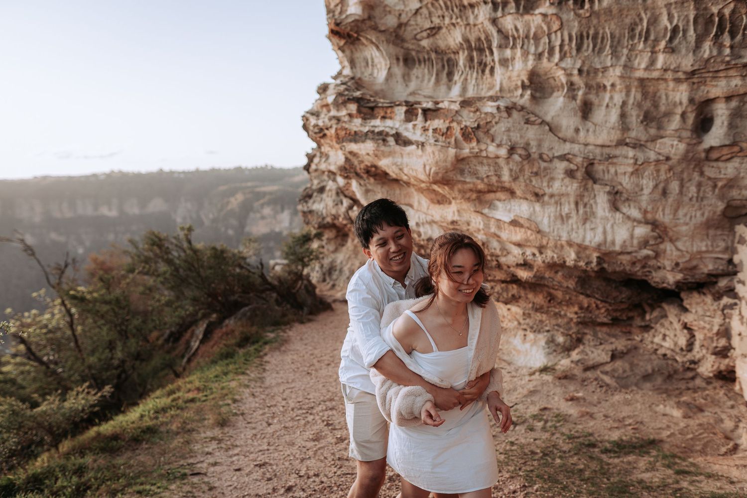 Two people sharing a playful moment on a mountain trail next to limestone cliffs.