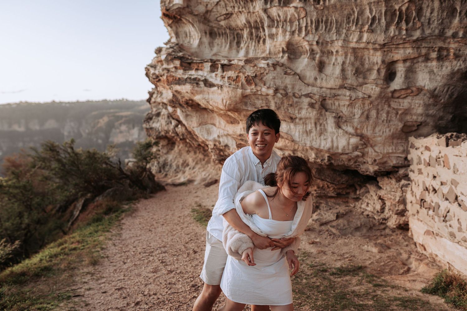 A sweet embrace captured on a scenic mountain trail with layered cliffs in the background.