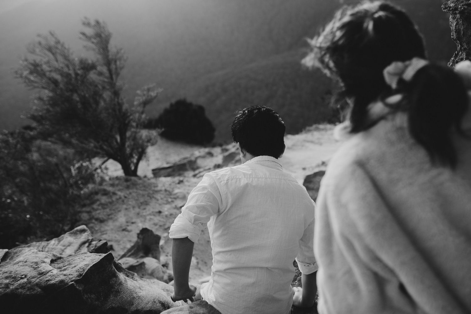 A black and white photo of two people sitting on a mountain overlook.