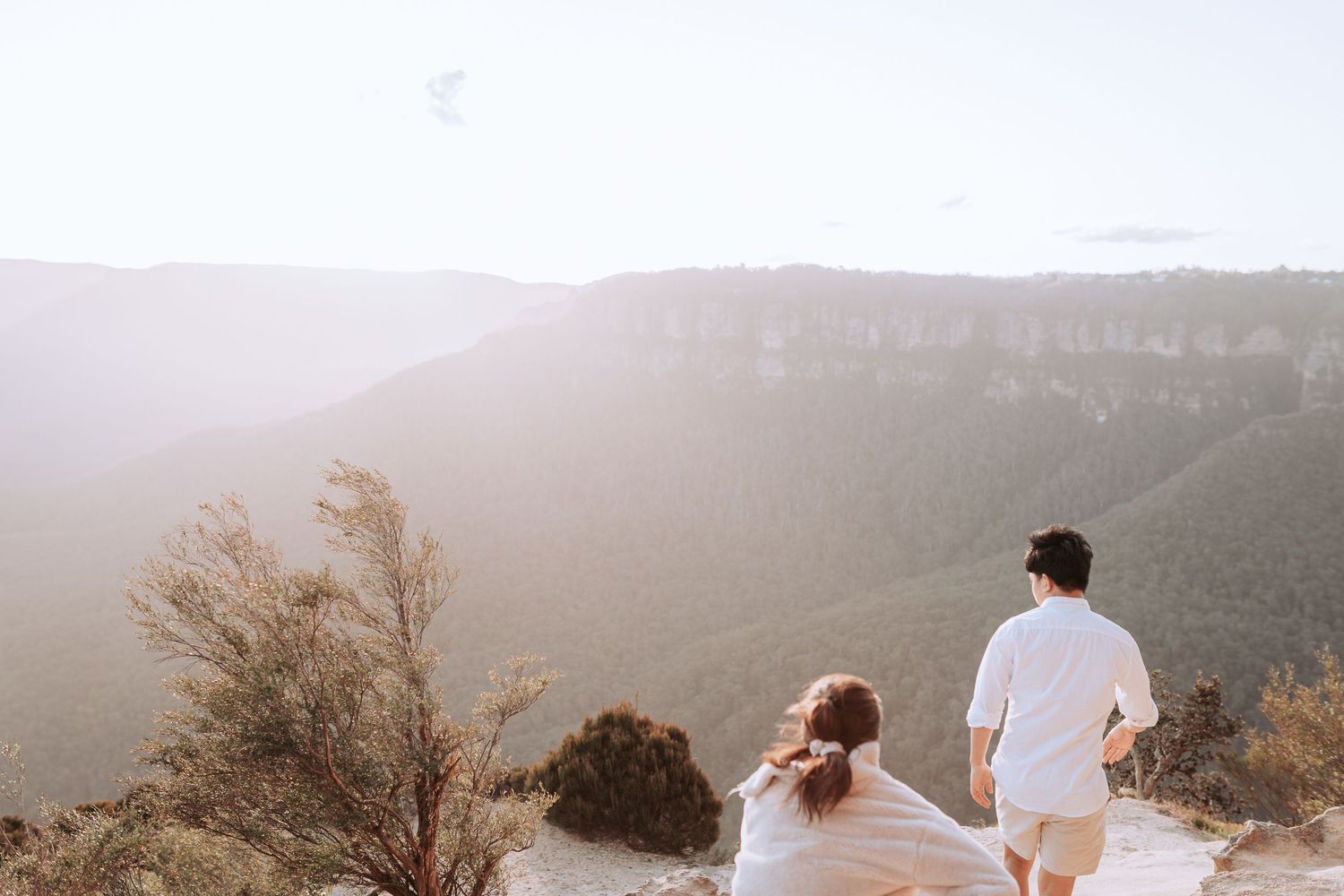 Two people in white clothing admiring a misty mountain landscape together.
