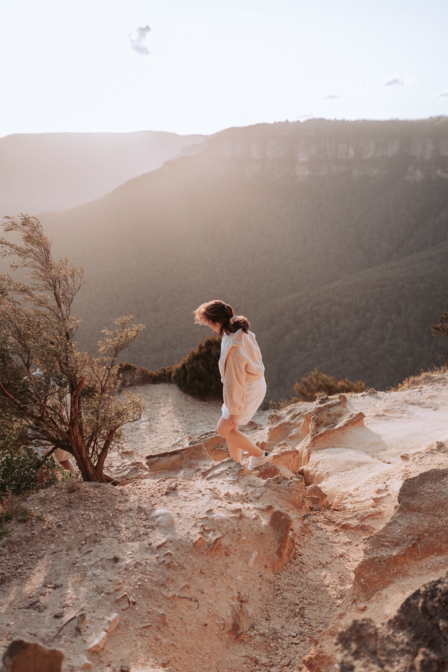 Two people in white attire exploring a rocky mountain ledge during golden hour.