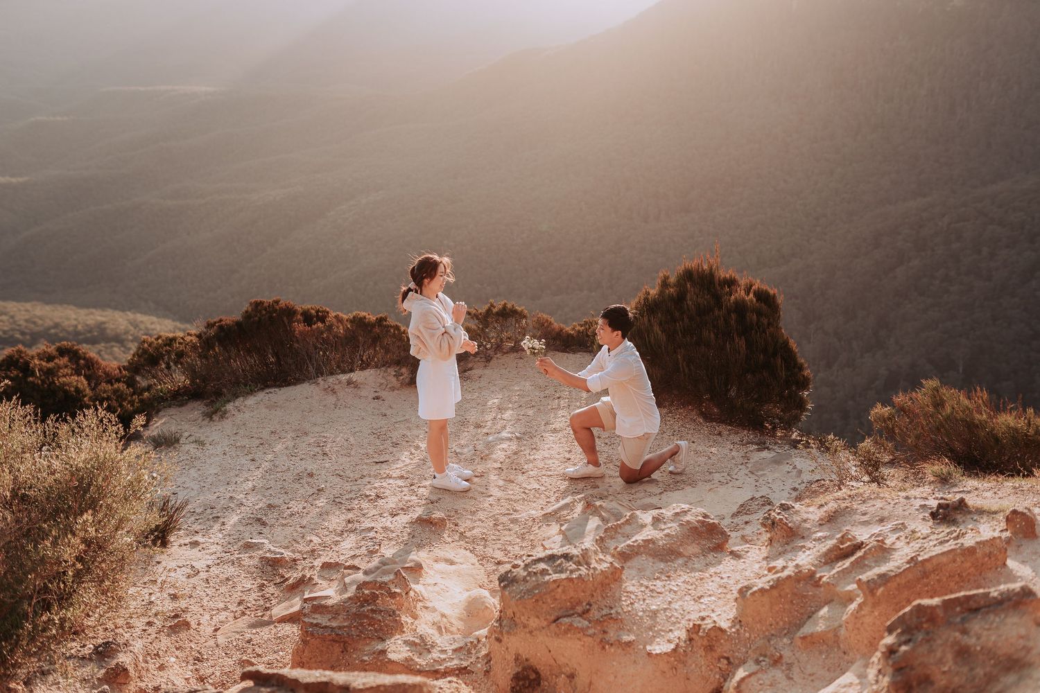 A couple sharing a special moment on a cliff edge during sunset in the mountains.
