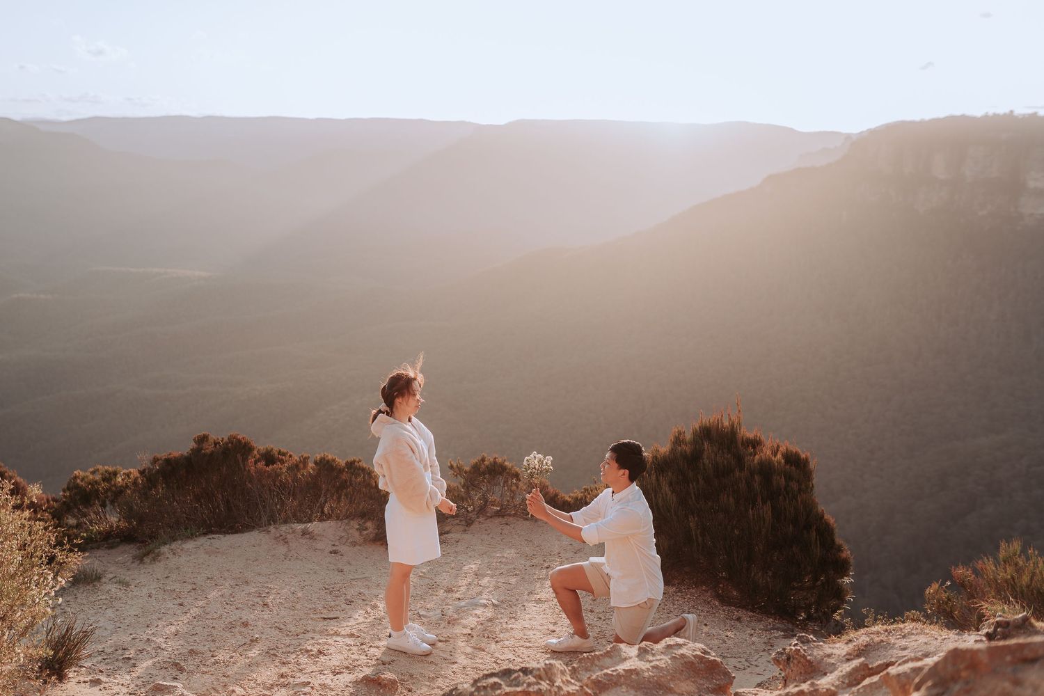 A romantic proposal scene at sunset on a mountain overlook with scenic valley views.