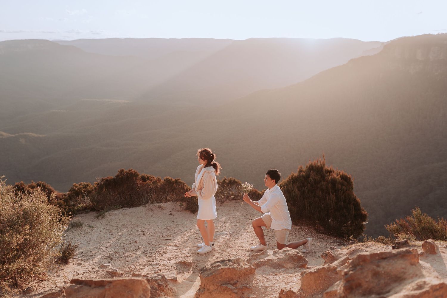 Two people sharing an emotional moment on a mountain cliff during sunset.
