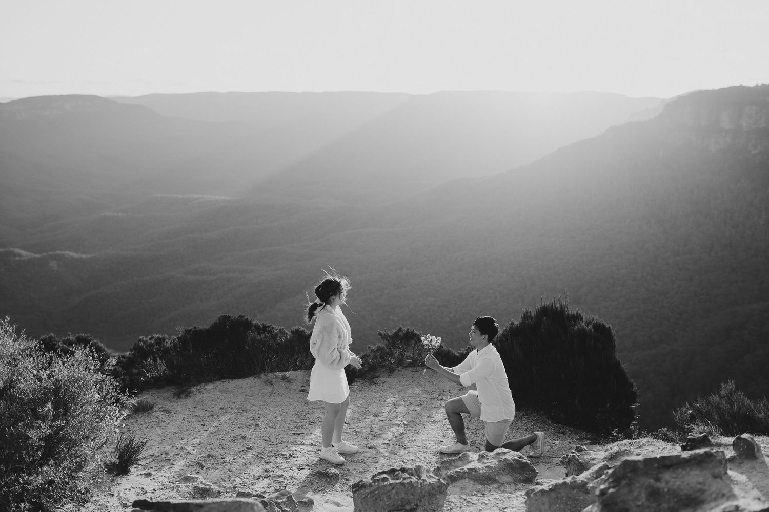 A black and white photograph of a proposal on a mountain overlook with valley views.